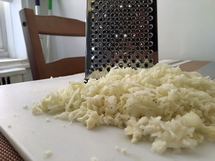 pile of cauliflower rice on a cutting board with box grater
